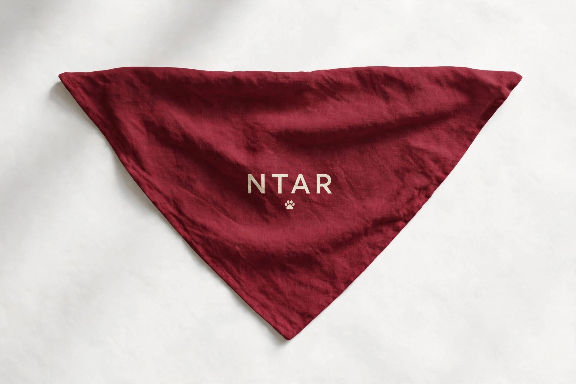 Wine-red dog bandana laid flat, with the NTAR name printed in cream above a small paw print